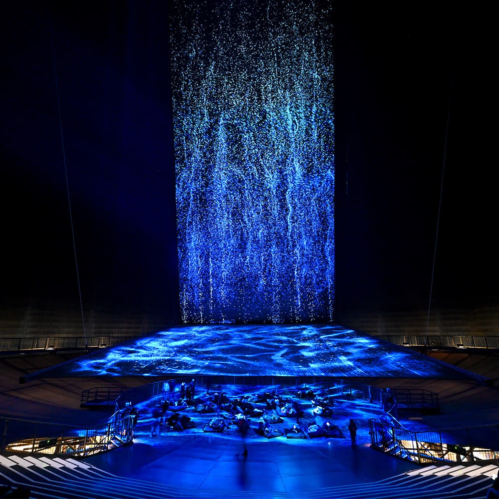 Zuschauerbereich vor "DIE WELLE" im Gasometer Oberhausen: blaue Lichtkaskade über kreisförmig angeordneten Sitzreihen