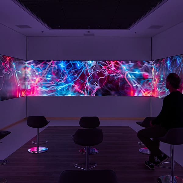 Person sitzt im abgedunkelten Infinity-Raum des Henkel Inspiration Center Z55 vor einer LED-Screen-Wand mit abstrakten, pink-blauen Visuals.
