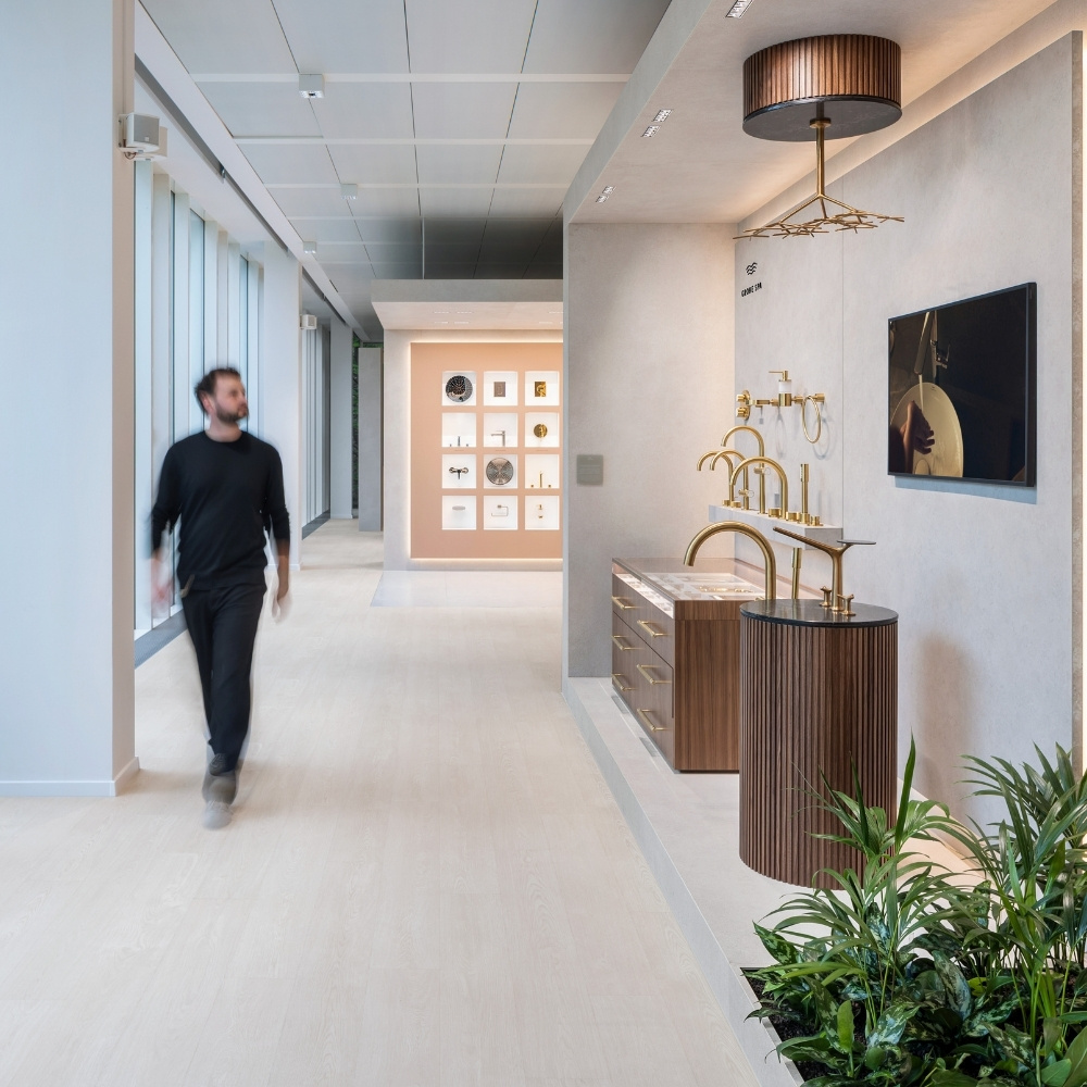 Besucher geht durch hellen Ausstellungsflur, rechts die GROHE SPA Inszenierung mit goldenen Armaturen und Monitor